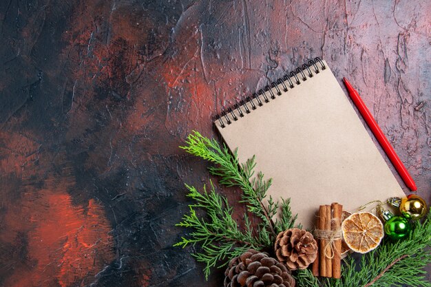 Top view pine tree branches and pinecones on a notebook red pen dried lemon slices on dark red surface free place