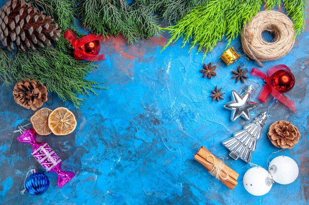 상위 뷰 소나무 나뭇가지 솔방울 짚 스레드 크리스마스 트리 장난감 아니스 씨앗 계피 스틱 파란색-빨간색 표면에 말린 레몬 조각
