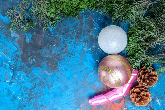 Top view pine tree branches pinecones xmas tree balls ribbon on blue-red surface