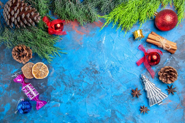 Top view pine tree branches pinecones xmas tree toys anise seeds dried lemon slices on blue-red surface