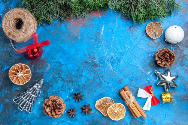 Top view pine tree branches straw thread cinnamon sticks dried lemon slices anise seeds xmas tree toys on blue-red surface