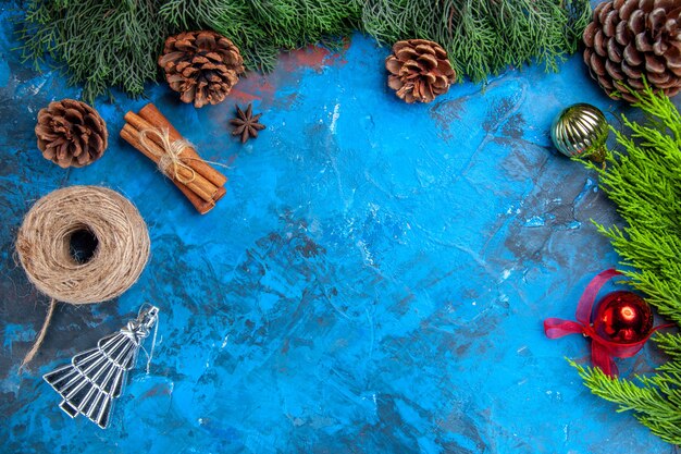 Top view pine tree branches straw thread cinnamon sticks xmas tree toys on blue-red background