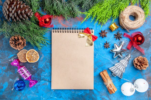 상위 뷰 소나무 나뭇가지 짚 실 크리스마스 트리 장난감 아니스 씨앗 계피 스틱 말린 레몬 조각 파란색-빨간색 배경에 작은 활이 있는 노트북