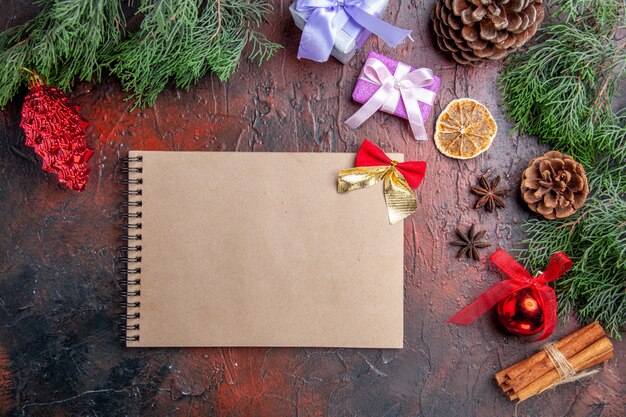 Top view pine tree branches with cones anises cinnamon xmas details a notebook on dark red background xmas photo