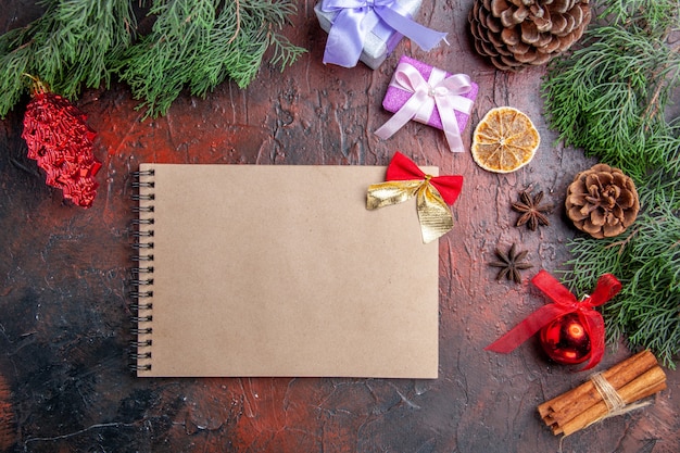 Top view pine tree branches with cones anises cinnamon xmas details a notebook on dark red surface