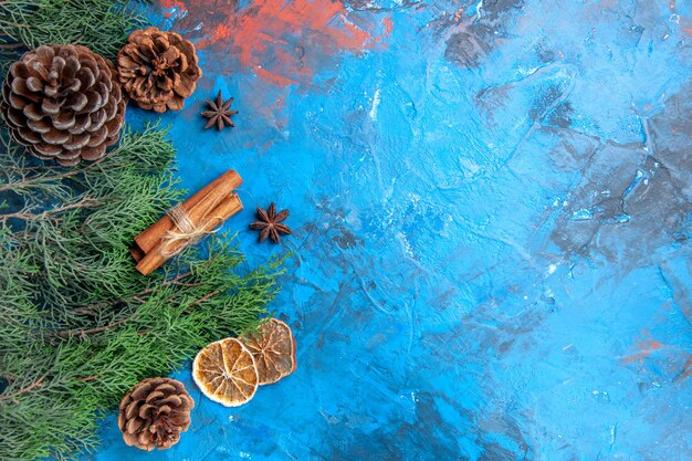 Top view pine tree branches with cones cinnamon sticks anise seeds dried lemon slices on blue-red surface