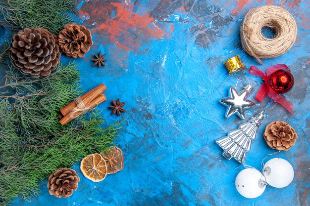Вид сверху сосновые ветки с шишками палочки корицы семена аниса сушеные ломтики лимона и вертикальные ряды соломенной нити рождественские елочные игрушки на сине-красном фоне с местом для копирования