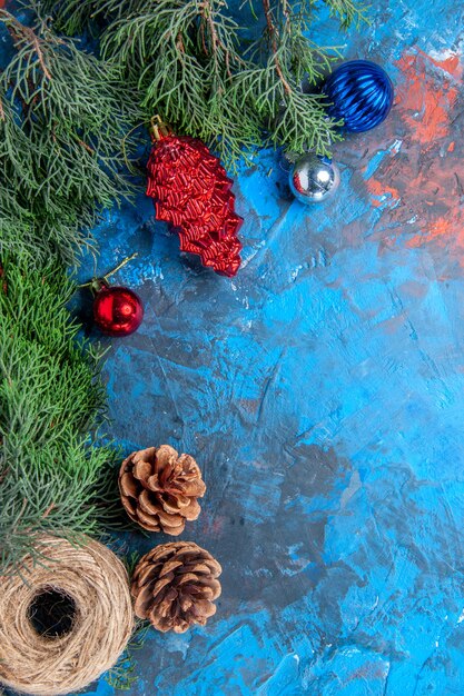 파란색-빨간색 표면에 솔방울과 화려한 크리스마스 장난감 짚 실이 있는 상위 뷰 소나무 가지