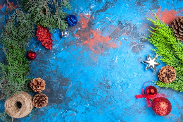 Top view pine tree branches with pinecones and colorful xmas tree toys straw thread on blue-red surface