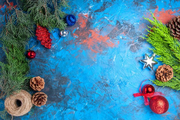 Top view pine tree branches with pinecones and colorful xmas tree toys straw thread on blue-red surface