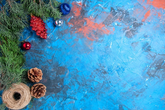 Top view pine tree branches with pinecones and colorful xmas tree toys straw thread on blue-red surface