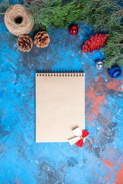 松ぼっくりとカラフルなクリスマスツリーのおもちゃと青赤の表面に弓とわら糸ノートブックの上面図松の木の枝
