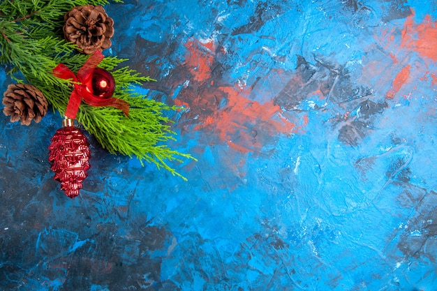 Top view pine tree branches with pinecones and hanging ornaments on blue-red background with free place