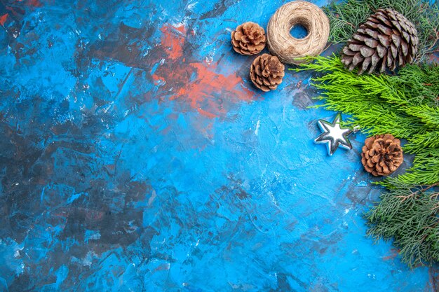 Vista dall'alto rami di pino con pigne filo di paglia stella natale ciondolo su sfondo blu-rosso con spazio libero