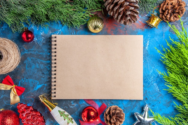 Top view pine tree branches with pinecones straw thread xmas hanging ornaments a notebook on blue-red surface