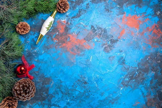 Вид сверху сосновые ветки с шишками, рождественские игрушки на сине-красной поверхности
