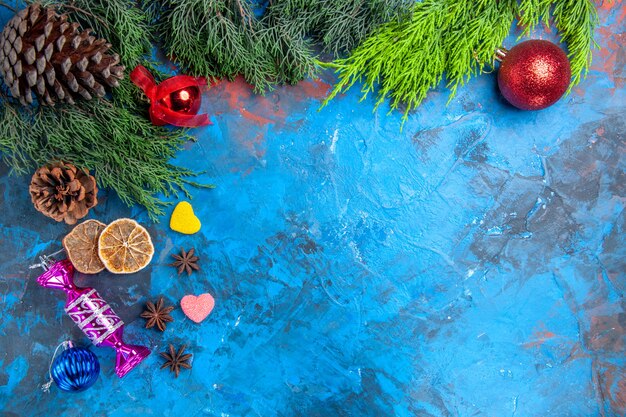 Top view pine tree branches xmas tree toys anise seeds dried lemon slices heart shaped candies on blue-red surface