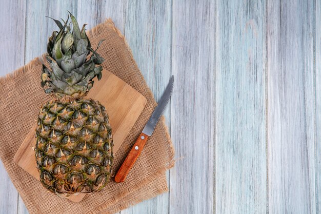 Free photo top view of pineapple on cutting board with knife on sackcloth and wooden surface