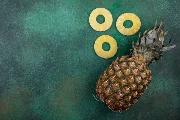 Free photo top view of pineapple and pineapple slices on green surface