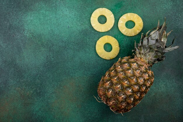 top view of pineapple and pineapple slices on green surface