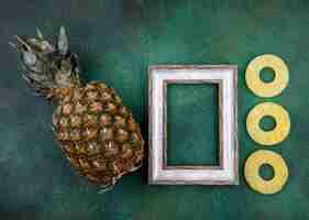 Free photo top view of pineapple and pineapple slices with frame on green surface