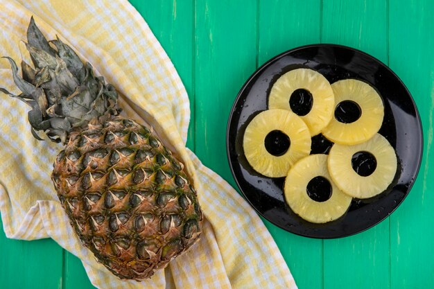 Foto gratuita vista dall'alto di ananas sul panno plaid con fette di ananas nel piatto sulla superficie verde