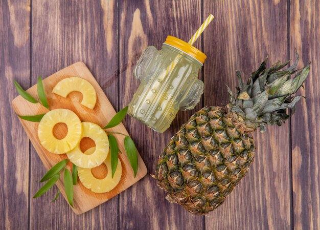 Top view of pineapple slices on cutting board with pineapple juice and pineapple on wooden surface