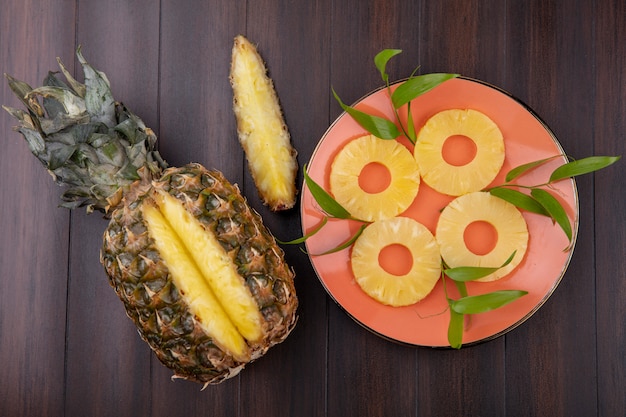 Top view of pineapple with one piece cut out from whole fruit with pineapple slices in plate on wooden surface