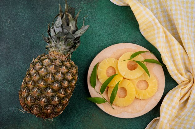 Top view of pineapple with pineapple slices on cutting board on green surface