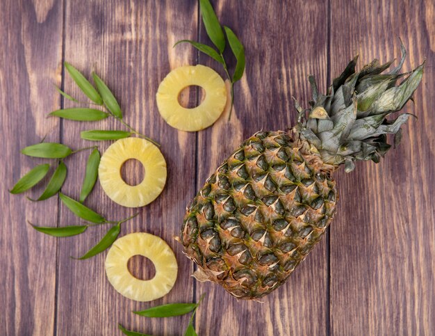 Top view of pineapple with pineapple slices and leaves on wooden surface