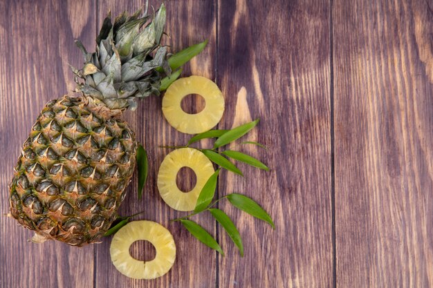 Top view of pineapple with pineapple slices and leaves on wooden surface