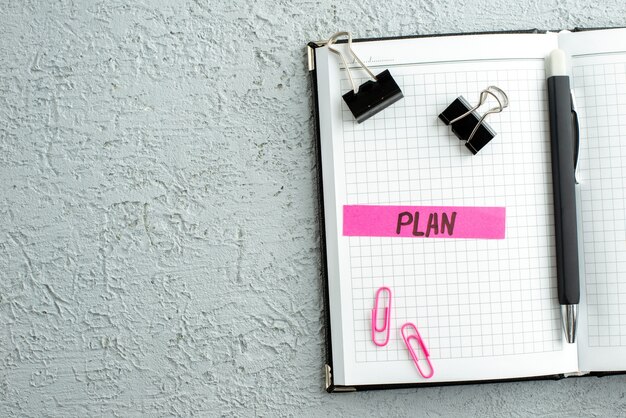 Top view of pink color plan writing pen and open spiral notebook on gray sand background