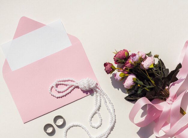 バラの花束の横にある結婚式の招待状のトップビューピンク封筒