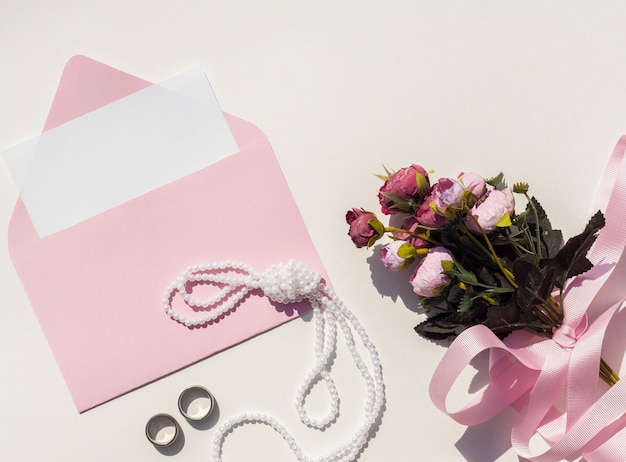 Top view pink envelope with wedding invitation next to bouquet of roses 