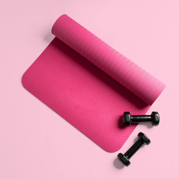 Вид сверху розового коврика для фитнеса и двух черных гантелей, изолированных на розовой поверхности