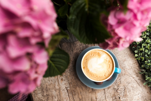 木の表面にピンクの花と泡立った泡とおいしいコーヒーのトップビュー