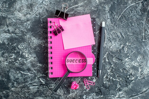top view pink notepad with staples pen magnifier and success note on gray background copybook school color college student business work job