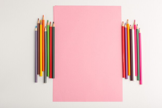 Top view pink paper blank with colorful pencils on white surface