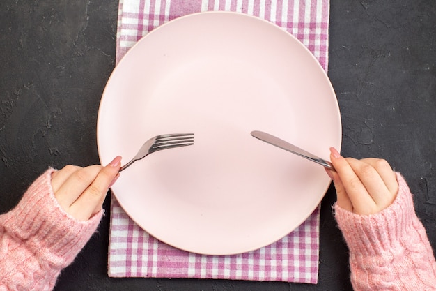 Top view pink plate with female holding fork and knife on dark surface