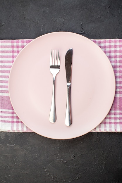 Top view pink plate with fork and knife on dark background