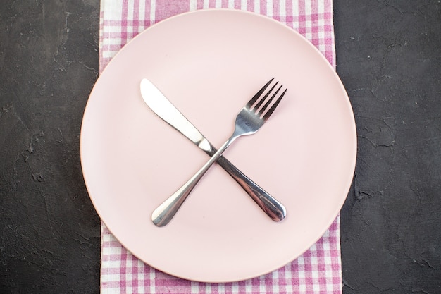 Вид сверху розовая тарелка с вилкой и ножом на темном фоне