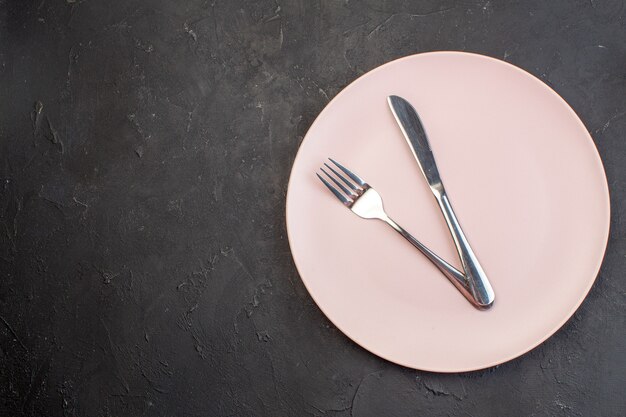 Вид сверху розовая тарелка с вилкой и ножом на темной поверхности