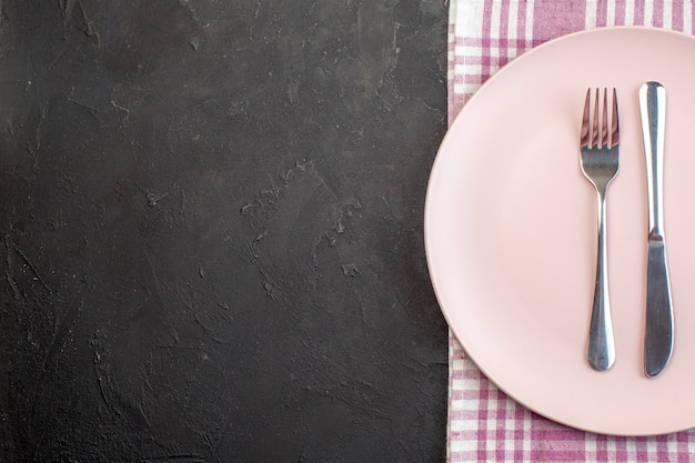 Top view pink plate with fork and knife on dark surface