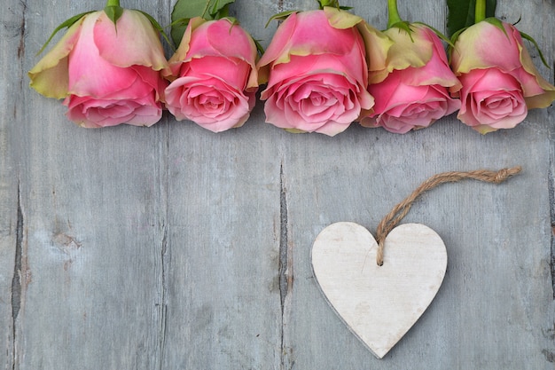 Top view of pink rose flowers with a heart wooden tag with space for text on a wooden surface