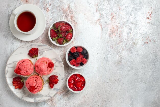 Top view of pink strawberry cakes with cup of tea on white surface