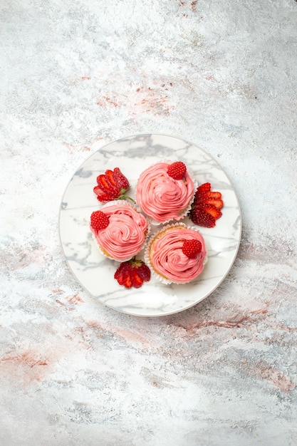 Top view of pink strawberry cakes with fresh red strawberries on a white surface