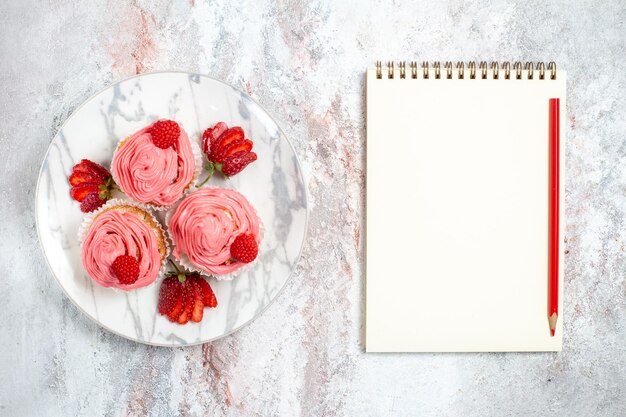 Вид сверху розовых клубничных пирогов со свежей красной клубникой на белой поверхности