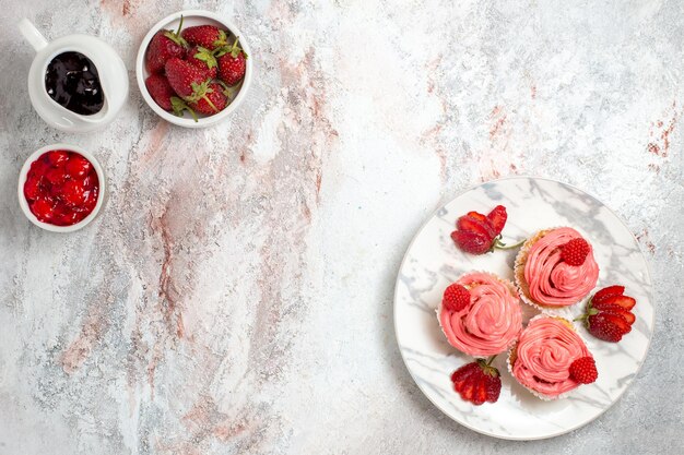 Top view of pink strawberry cakes with jam and chocolate bars on the white surface