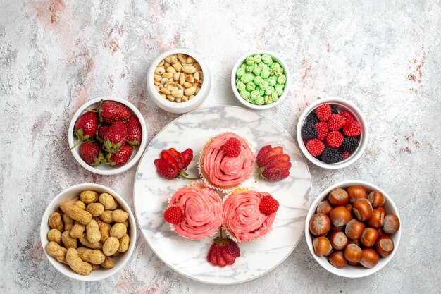 Top view of pink strawberry cakes with nuts and candies on white surface