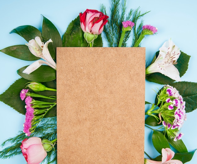 Top view of pink and white color roses and alstroemeria flowers with turkish carnation and statice with a brown sheet of paper on blue background